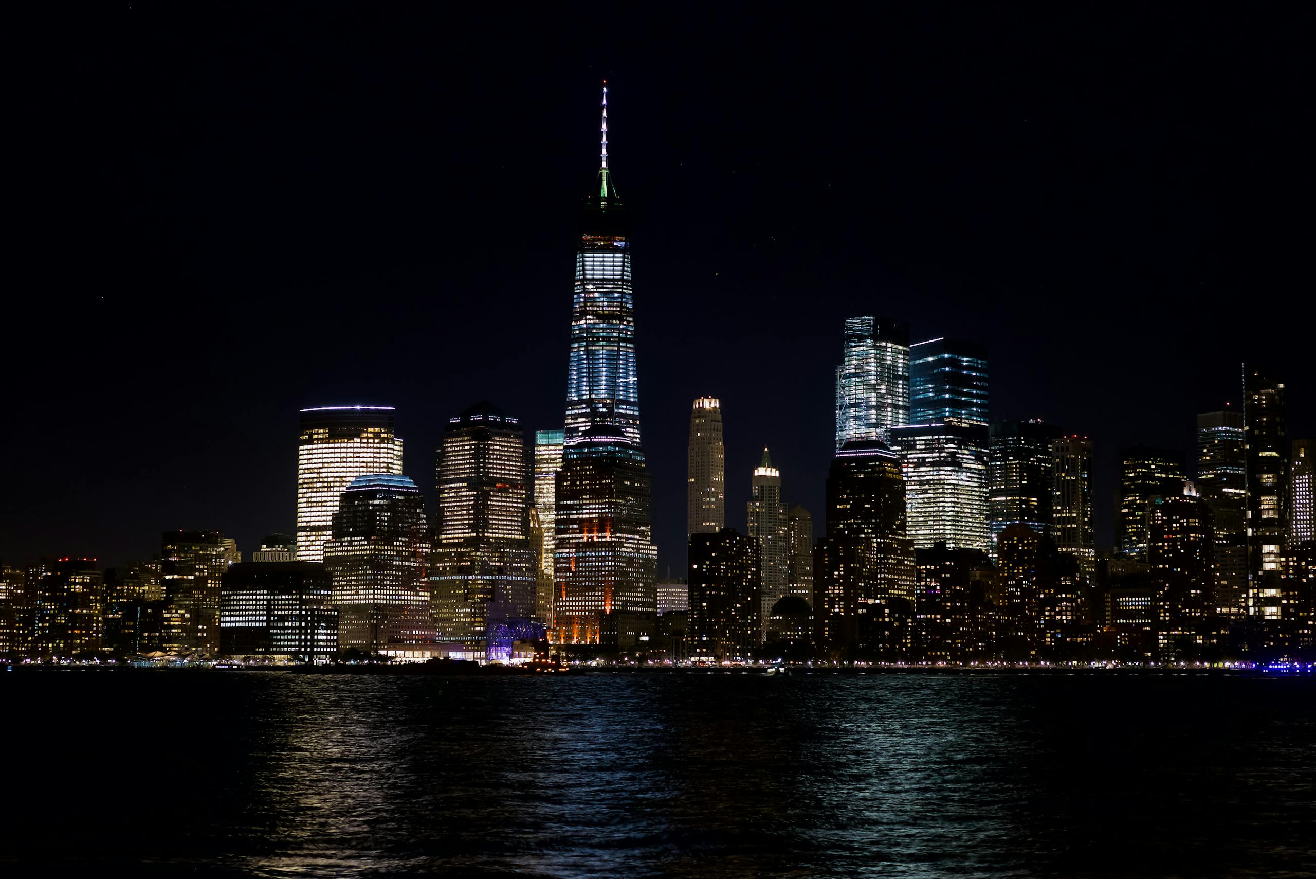 Illuminated skyline of New York City with iconic skyscrapers reflecting on the water.